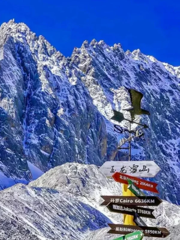 Jade Dragon Snow Mountain rkl5rfkp3vprzgibctcrj4p0fbtdq7y7oikrbr6kow 雲南麗江著名的 玉龍雪山 壯麗雪峰景觀。高聳陡峭的雪山覆蓋著白雪,在湛藍天空下顯得格外壯觀。前景是一個寫著「玉龍雪山」的方向指示牌與風向標,指向世界多個城市距離,為畫面增添旅遊地標特色,展現出這座著名雪山的雄偉與魅力。