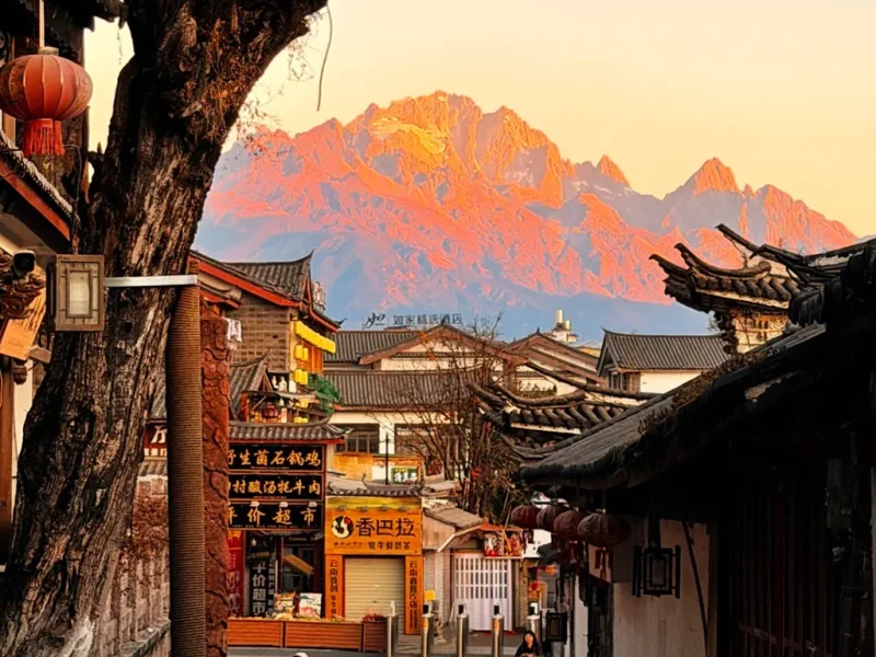 Lijiang Old Town 清晨的 麗江古城,傳統瓦屋、靜謐石板巷道,遠方是被晨光染金的玉龍雪山。