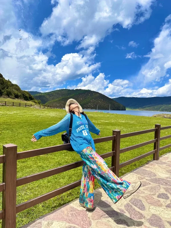 在普達措屬都湖的草原邊，靠著木柵欄張開雙臂，藍天白雲、草原湖泊相映，是香格里拉最自由的高原瞬間。