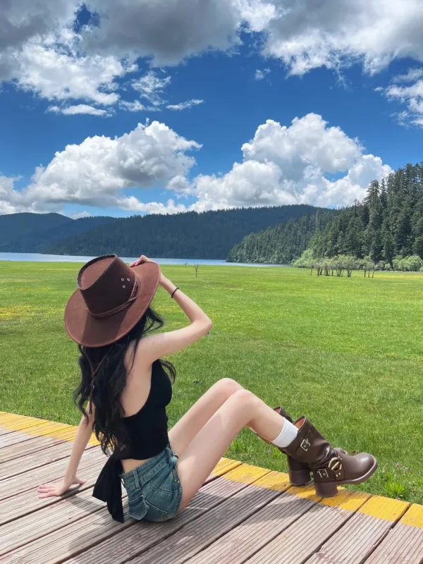 在普達措屬都湖的草原上，戴著牛仔帽坐在木棧道上，綠草如茵、湖泊森林相映，是香格里拉最清新的森林草原畫面。