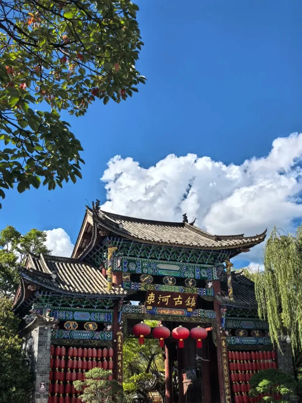 Shuhe Ancient Town Lijiang 3 麗江束河古鎮的牌樓,彩繪木雕與紅燈籠相映,藍天白雲下,是古鎮最具儀式感的入口畫面。